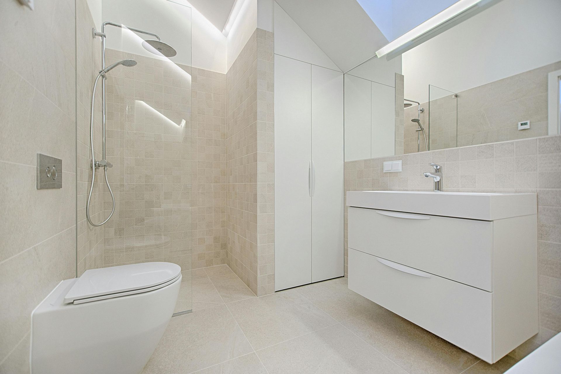 Salle de bain moderne avec douche, toilettes, vanité et armoire, le tout en blanc et beige.