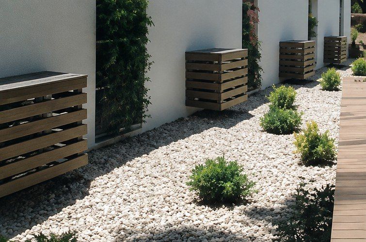 Patio moderno con una zona de grava, arbustos pequeños, paredes blancas y jardineras de listones de madera junto a una terraza
