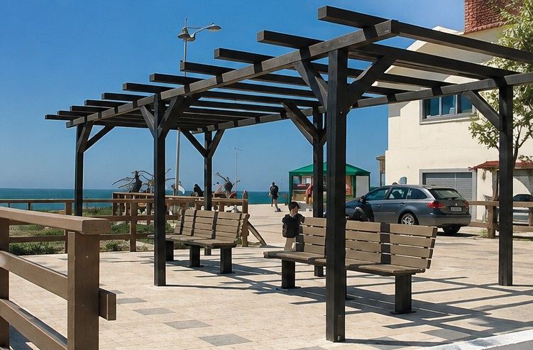 Paseo marítimo con bancos y pérgolas junto a un edificio y un coche aparcado