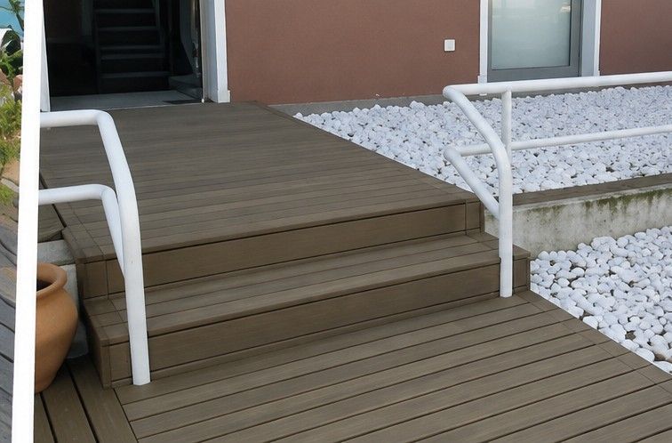 Escalera de madera con barandillas blancas que conduce a la entrada de una casa, junto a un camino de grava.