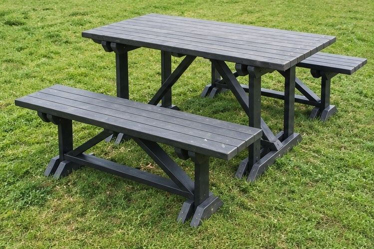 Mesa de pícnic de madera oscura con bancos sobre el césped, en un entorno al aire libre.