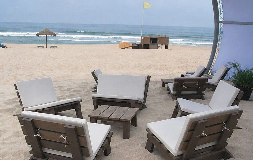 Tumbonas frente al mar bajo una pérgola con sombra, en una playa de arena.