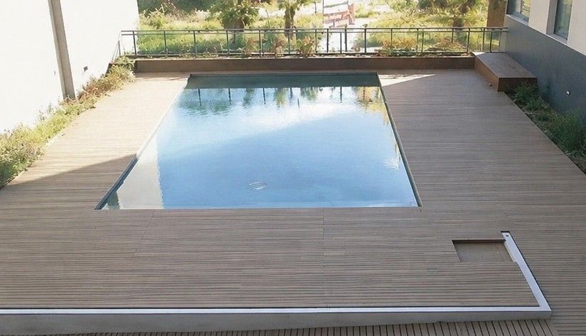 Jardín moderno con una piscina rectangular rodeada de una tarima de madera y un borde blanco