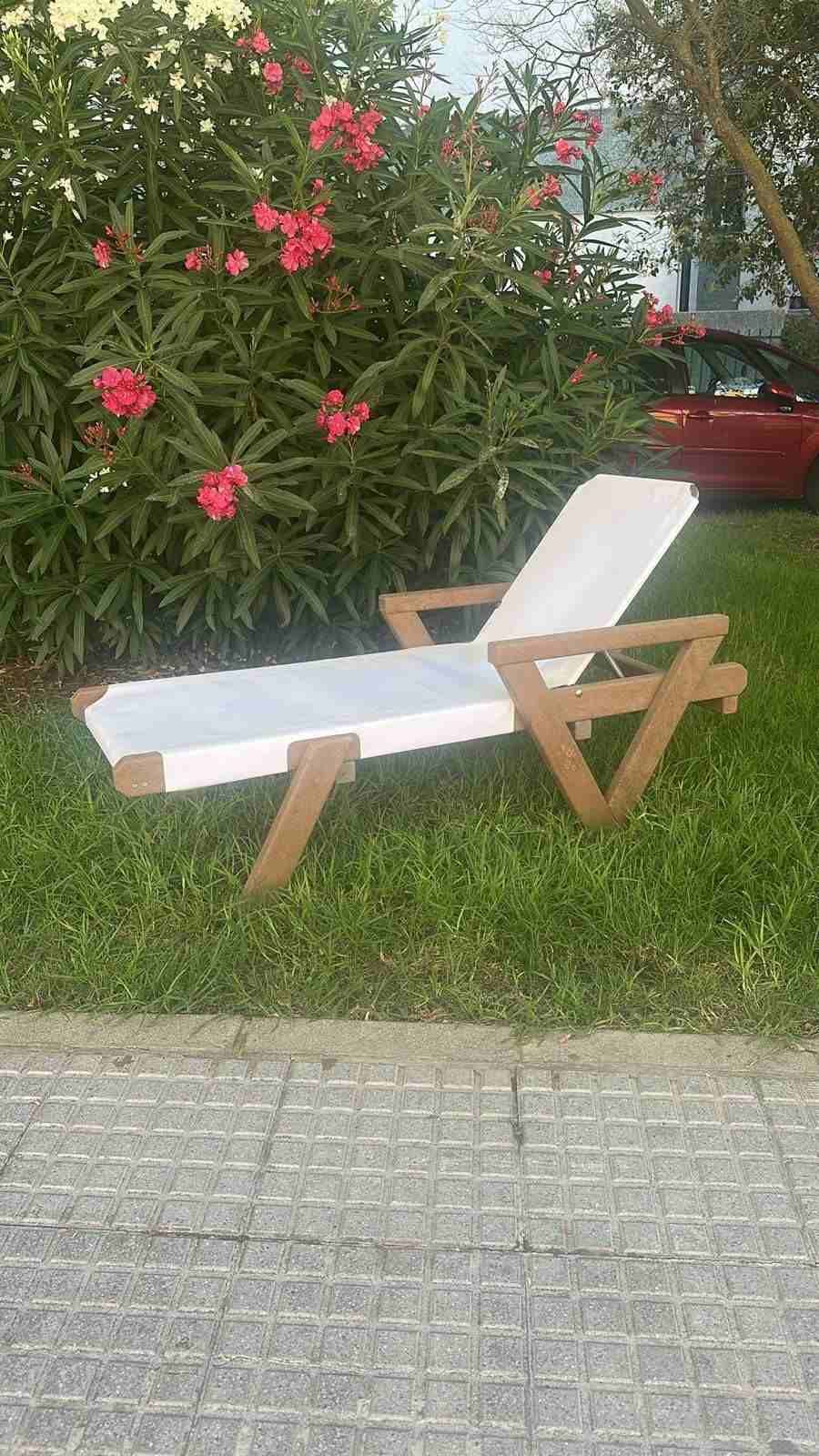 Sillón blanco de estructura de madera sobre el césped, junto a arbustos en flor