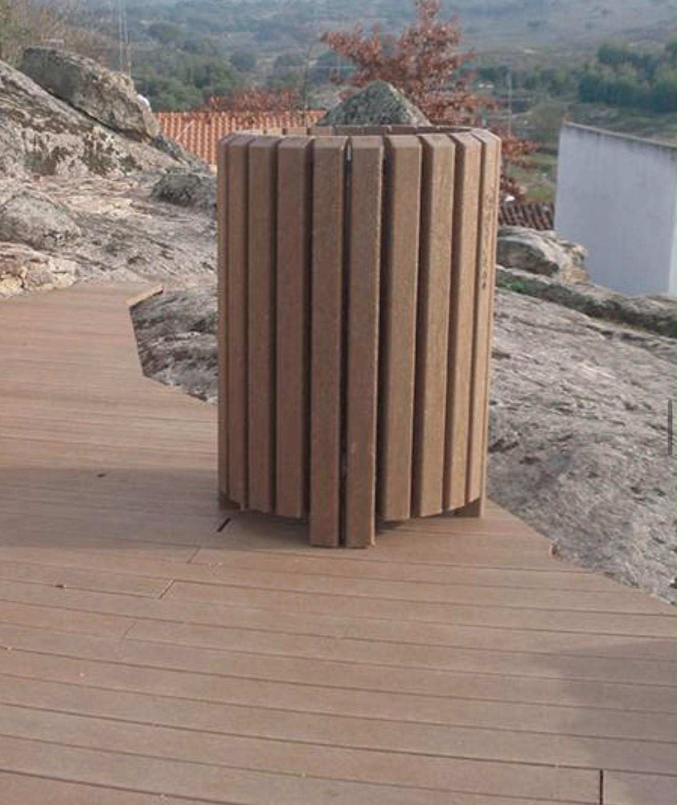 Papelera de listones de madera en una terraza con vistas a un mar rocoso y un paisaje lejano.