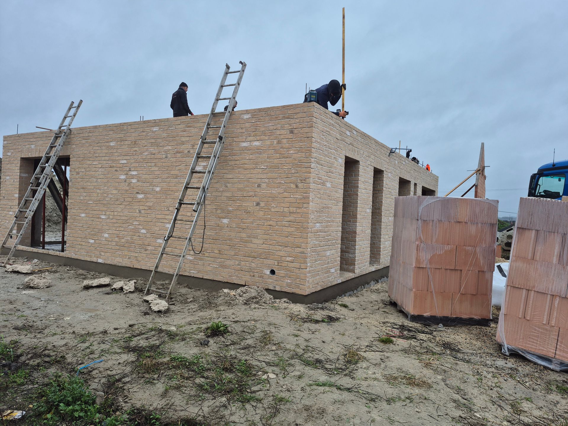 Des ouvriers du bâtiment se trouvent sur le toit d'un immeuble en briques d'un étage en construction, des échelles appuyées contre les murs.