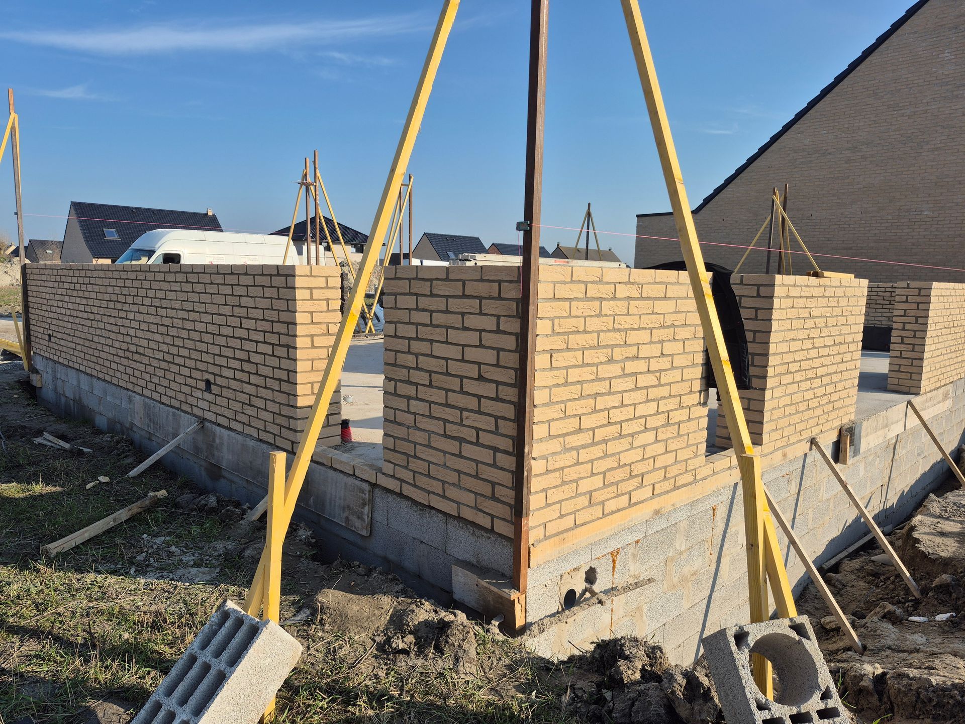 Chantier de construction montrant des murs en briques à moitié construits sur des fondations en béton.