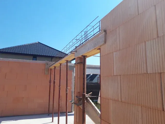 Un chantier de construction avec des murs en blocs, des vérins de soutien en acier et des barres d'armature métalliques apparentes.