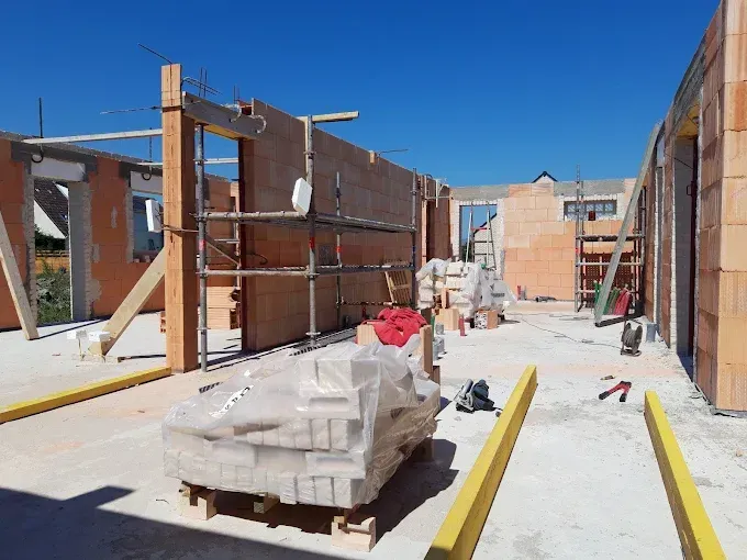 Un chantier de construction avec des murs en briques, un tas de matériaux au sol et des barrières de sécurité.