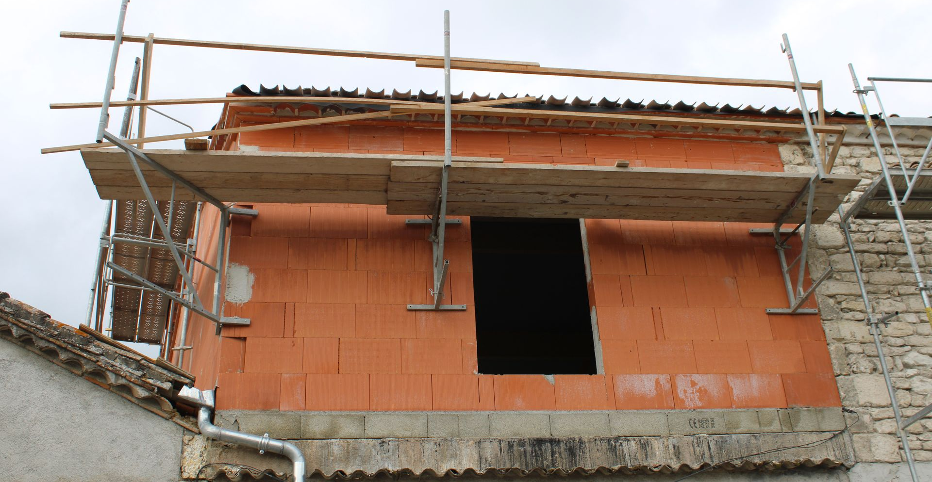 Un mur extérieur en briques d'argile est en construction, avec des échafaudages en bois fixés au bâtiment.