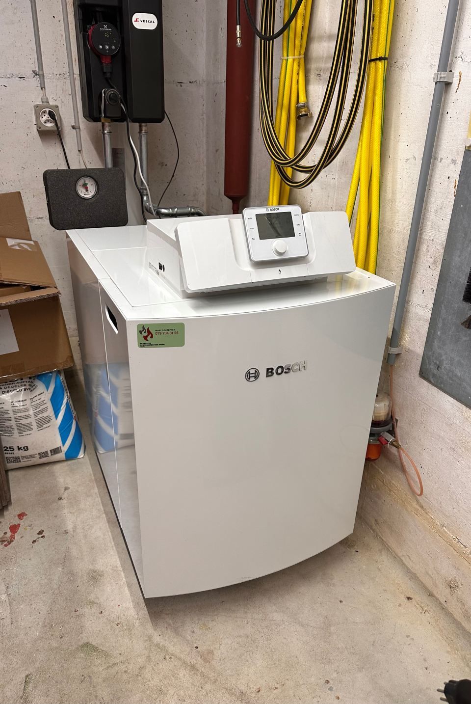 In einem Raum steht ein weisser Boiler neben einem gelben Schlauch. Foto von der Schrepfer Heizungstechnik GmbH