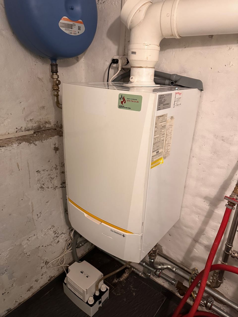 Ein weisser Heizkessel steht in einem Raum neben einer Wand. Foto von der Schrepfer Heizungstechnik GmbH