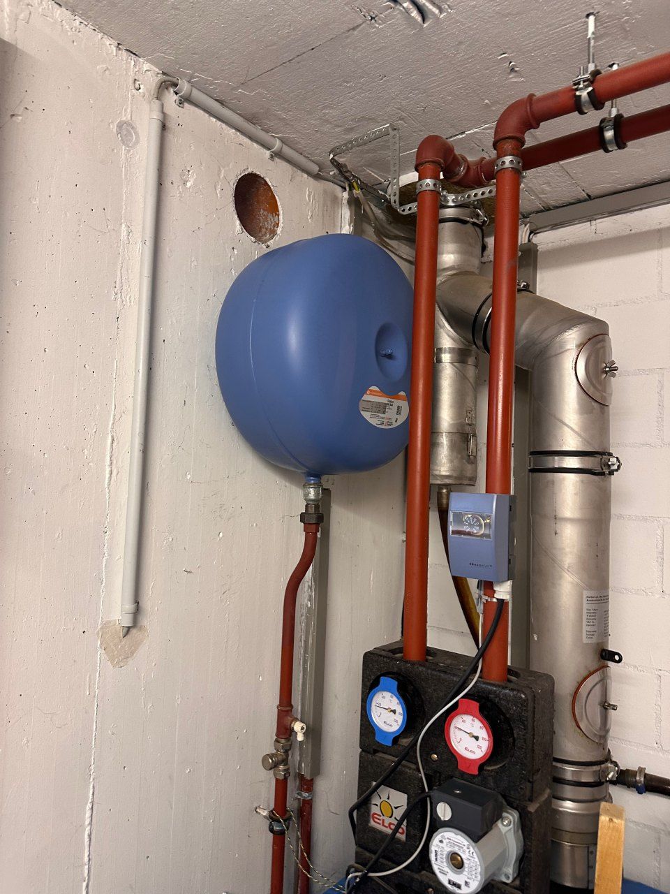 Ein Raum mit Rohren und einem blauen Tank an der Wand. Foto von der Schrepfer Heizungstechnik GmbH