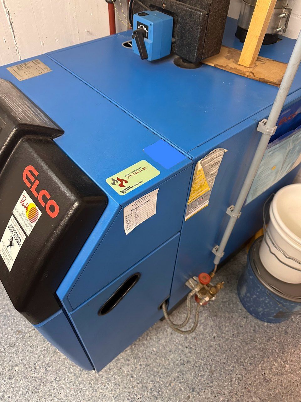 Ein blauer Elco-Kessel steht auf dem Boden neben einem Eimer. Foto von der Schrepfer Heizungstechnik GmbH