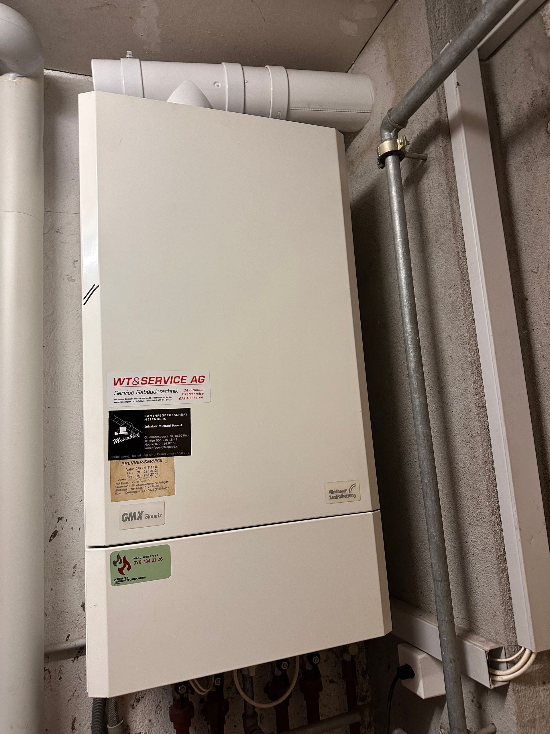 Ein weisser Kessel hängt neben Rohren an einer Wand. Foto von der Schrepfer Heizungstechnik GmbH