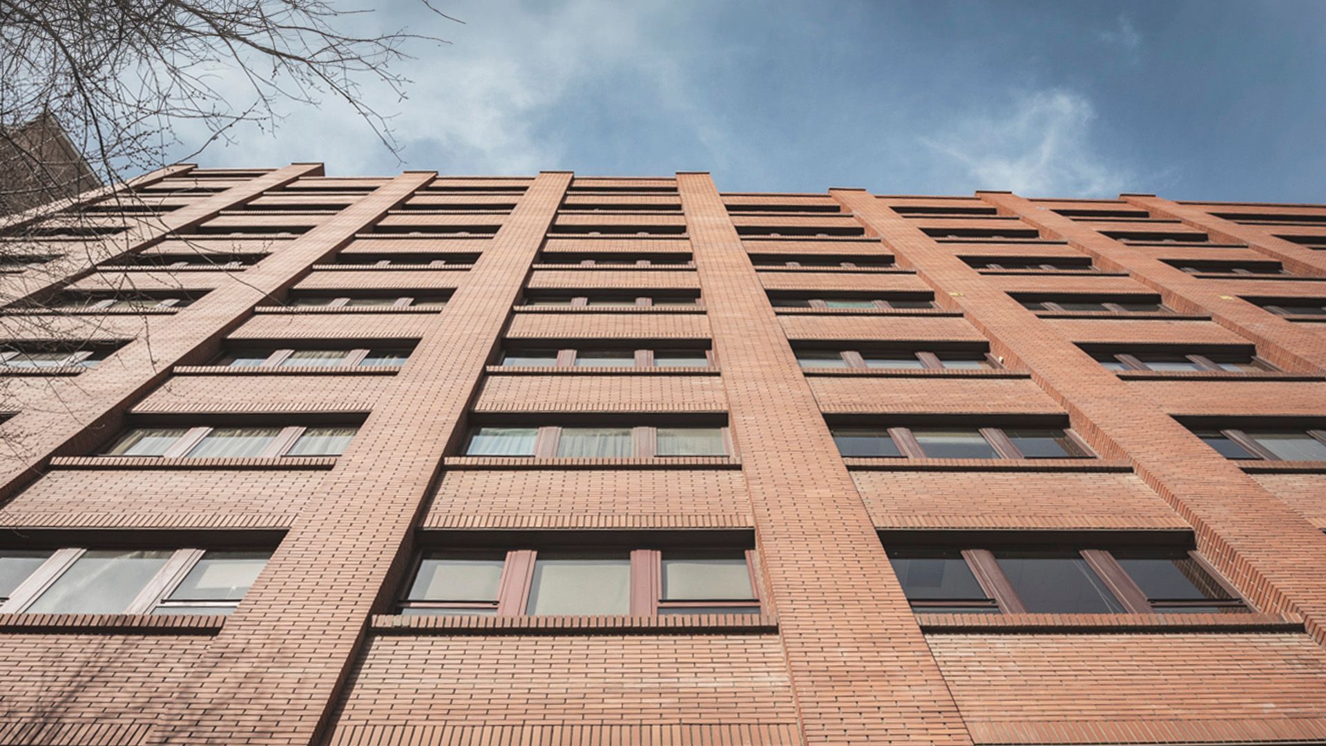 Mirando hacia arriba a un alto edificio de ladrillos con muchas ventanas.