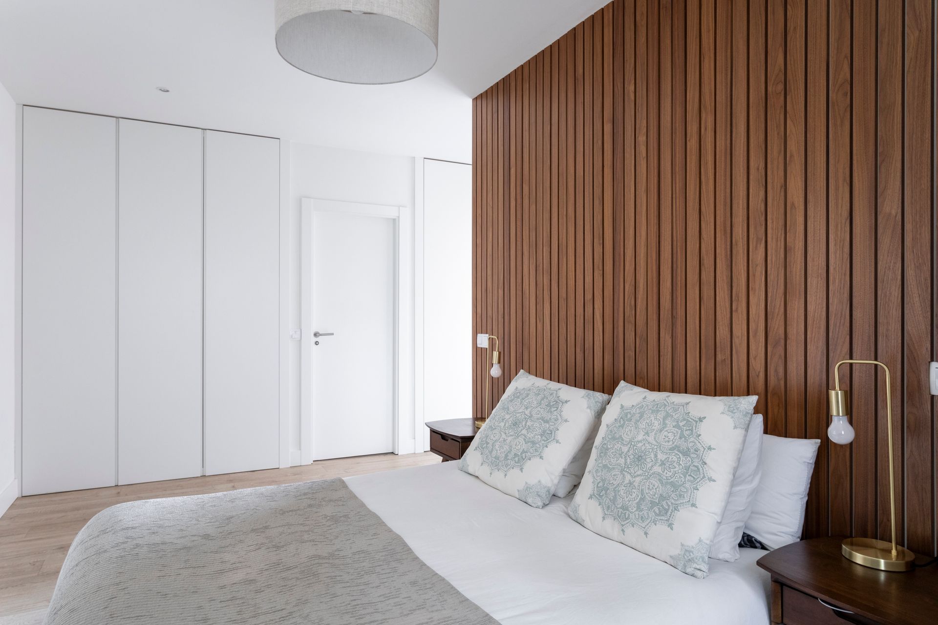 Un dormitorio con cama, mesita de noche, lámpara y pared de madera.