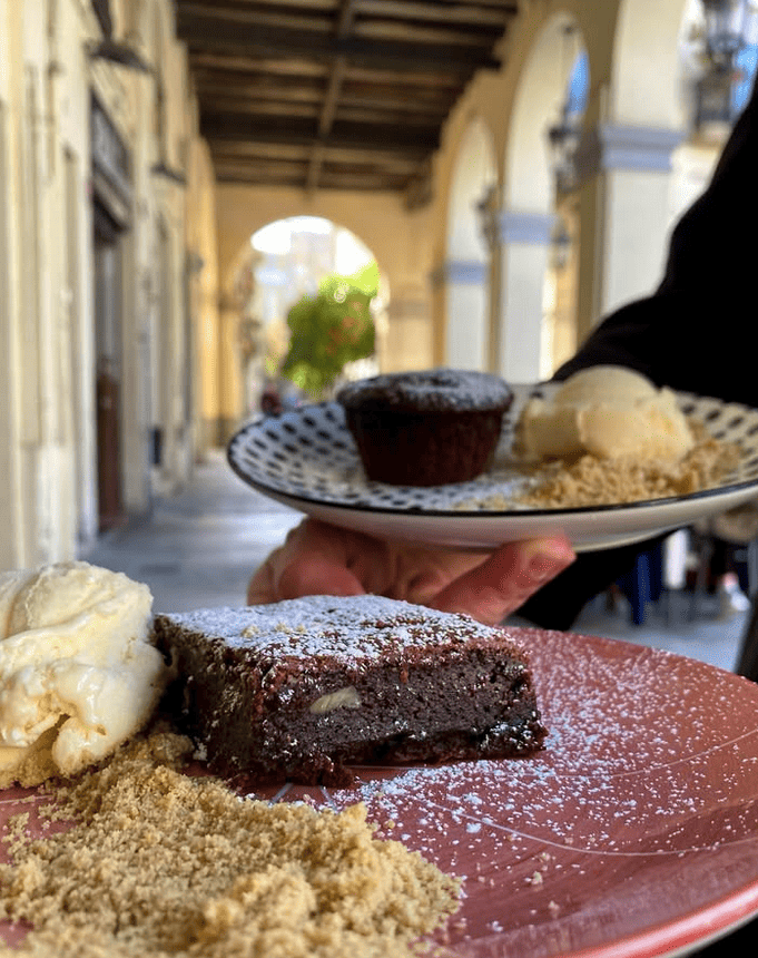 Una persona sostiene un plato de comida con un brownie y helado encima.