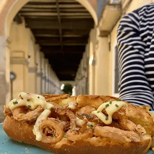 Una persona sostiene un sándwich con calamares y mayonesa encima.