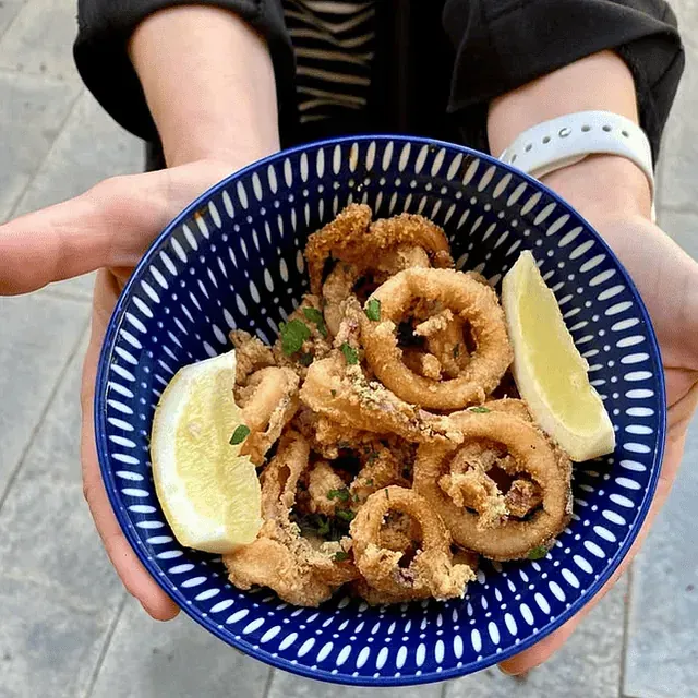 Una persona sostiene un tazón de calamares fritos y rodajas de limón.