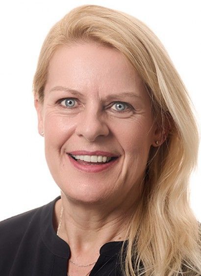 Eine Frau mit blonden Haaren und blauen Augen lächelt in die Kamera.