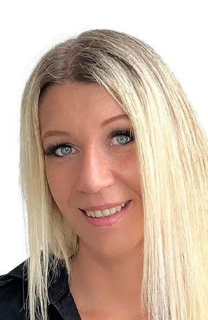 Eine Frau mit langen blonden Haaren und blauen Augen lächelt in die Kamera.