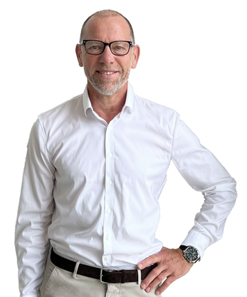 Ein Mann mit Brille und weißem Hemd steht mit den Händen in den Hüften da.
