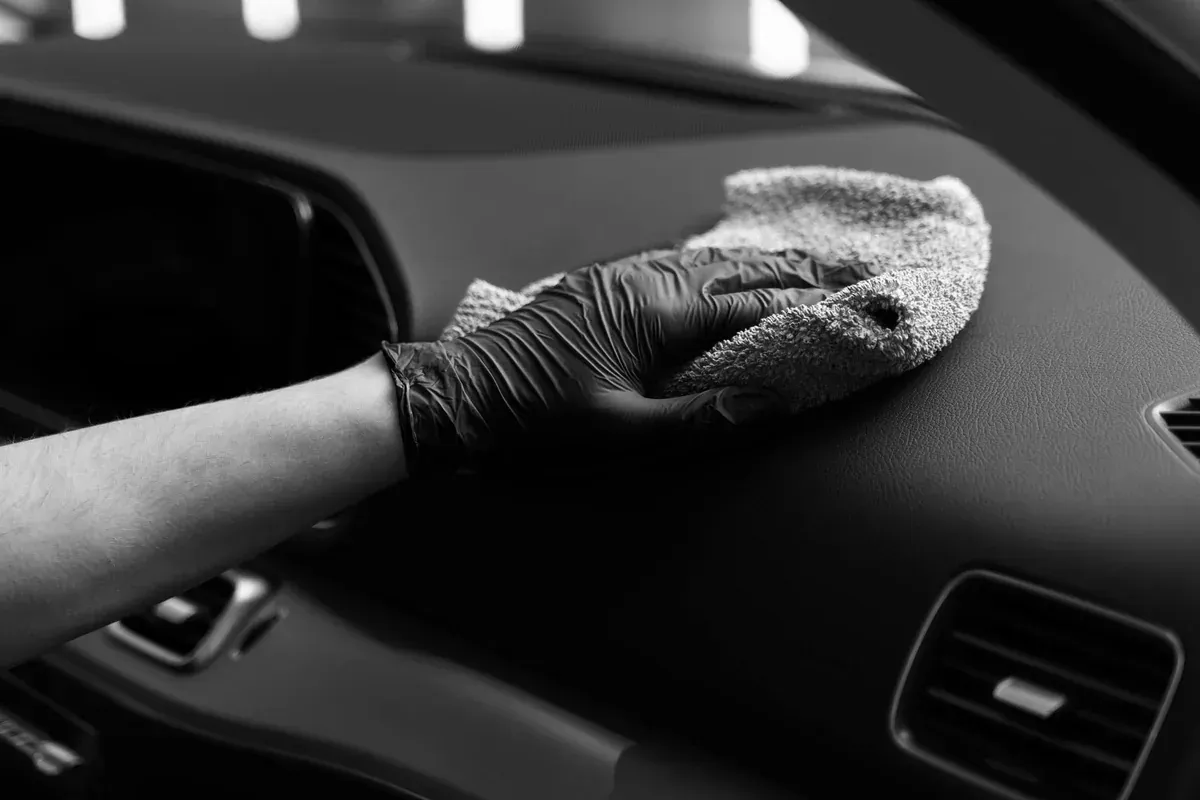 Mano enguantada limpiando el salpicadero de un coche con un paño de microfibra.