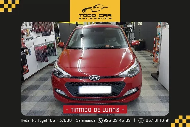 Hyundai i20 rojo con lunas tintadas, frente a la tienda "Todo Car Salamanca". El texto incluye dirección y números de teléfono.