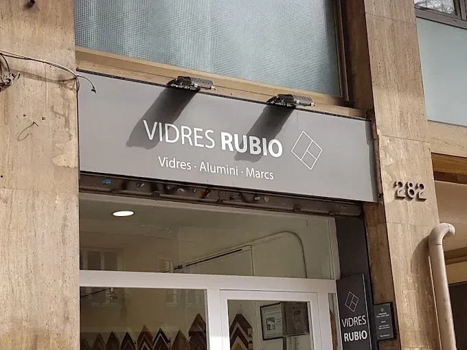 Letrero de la fachada de “VIDRES RUBIO”, una tienda de vidrio, aluminio y marcos ubicada en un edificio de madera.