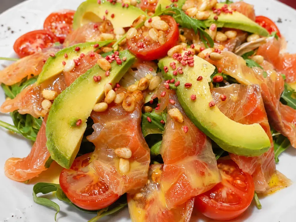 Ensalada de salmón, aguacate, tomate y nueces con semillas de sésamo y hojuelas de pimiento rojo.