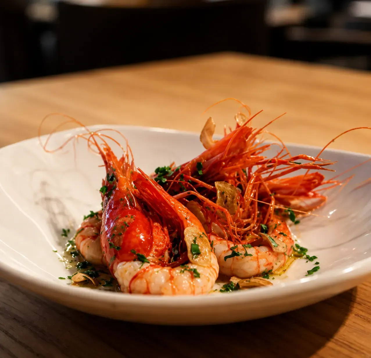 Bol blanco con gambas a la parrilla, hierbas y guarnición roja sobre una mesa de madera.