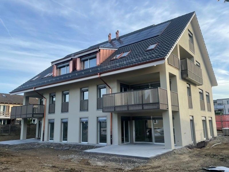 Zweistöckiges modernes Gebäude mit Balkonen und Solarzellen auf dem Dach unter blauem Himmel.