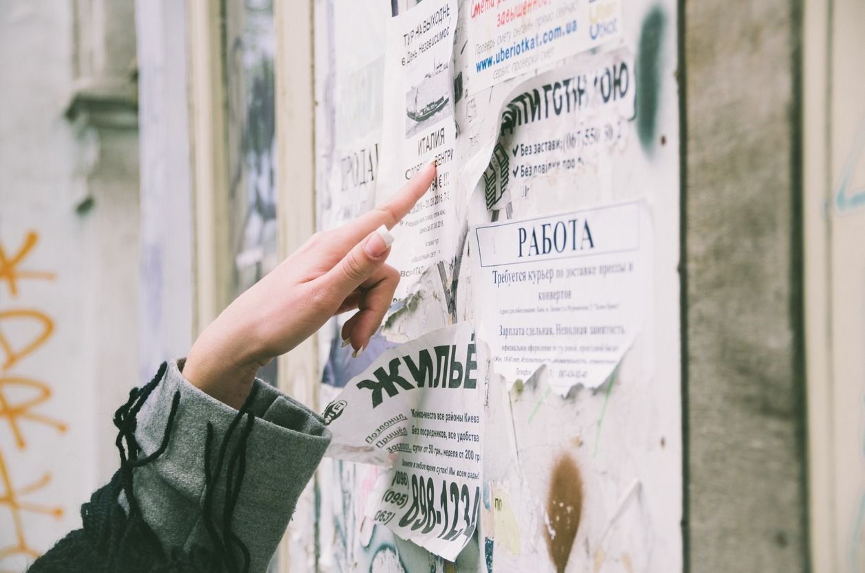 Una mano apuntando hacia un tablón de anuncios cubierto de carteles desgastados y anuncios al aire libre.