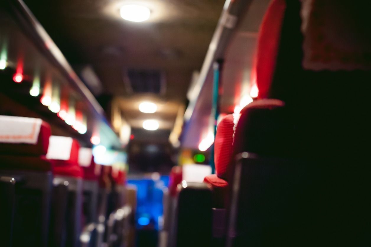 Dentro de un autobús, asientos rojos se alinean a ambos lados del pasillo, con luces encima.