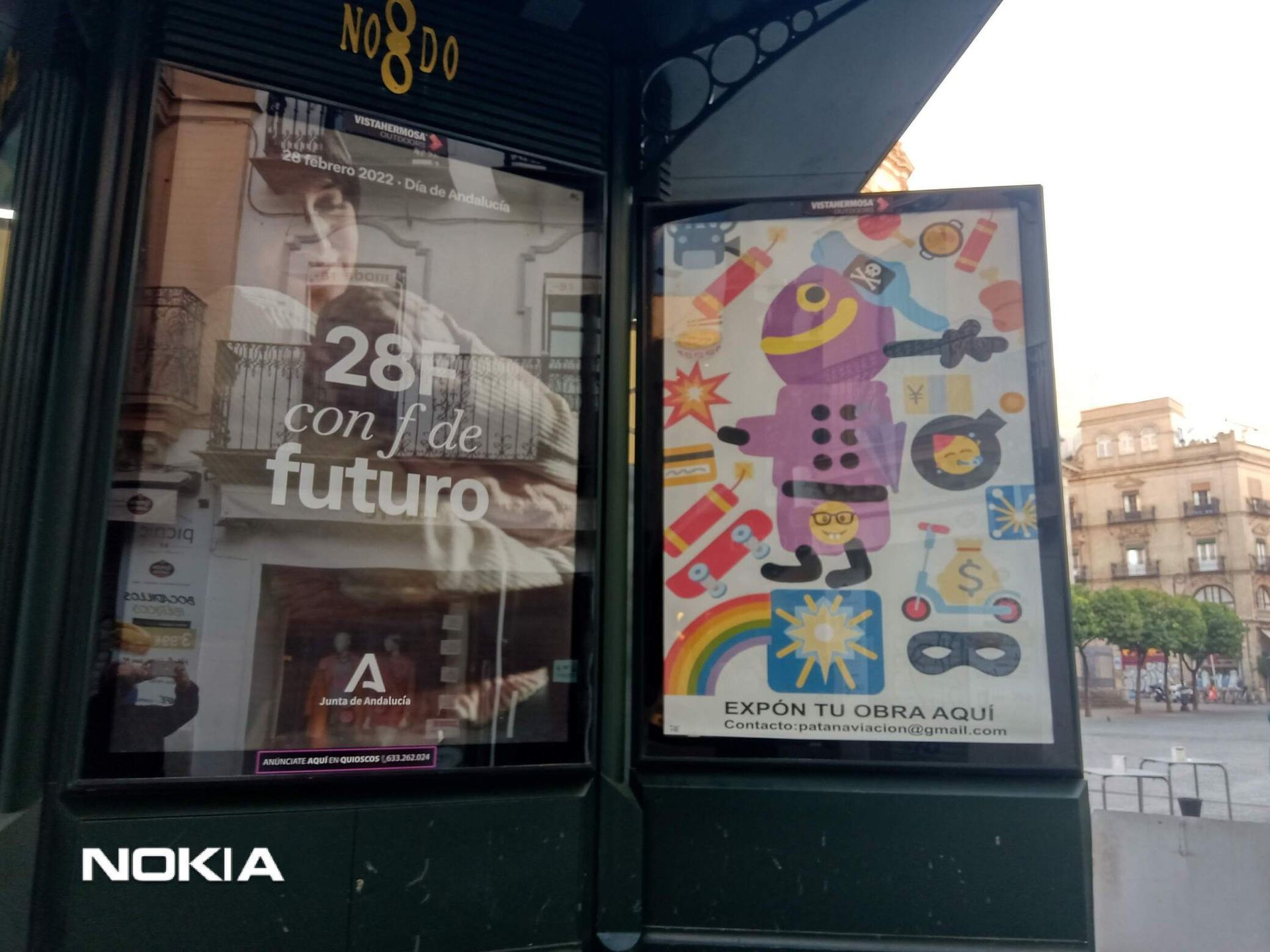 Dos carteles: uno con una persona y un texto, el otro con un robot de dibujos animados y objetos coloridos, en una esquina de la calle.