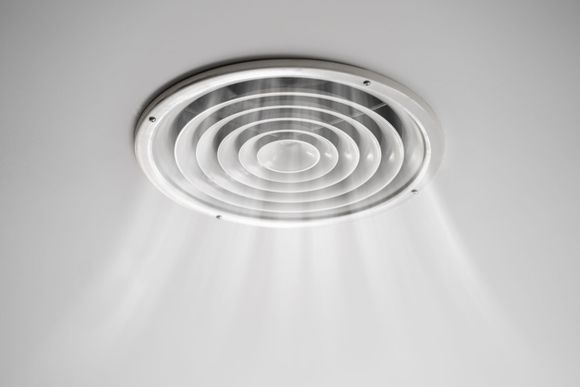 Grille d'aération blanche au plafond, munie d'anneaux concentriques diffusant des faisceaux lumineux sur un plafond uni.