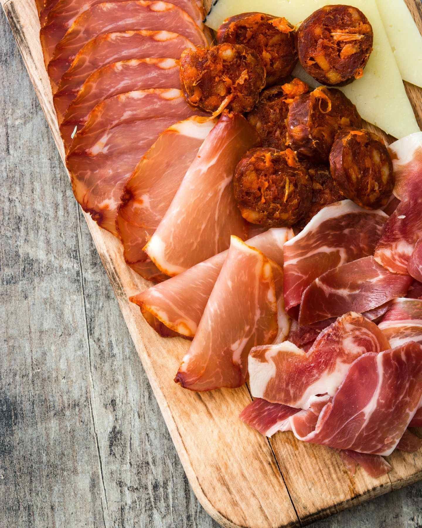 Una tabla de cortar de madera cubierta con una variedad de carnes y quesos.