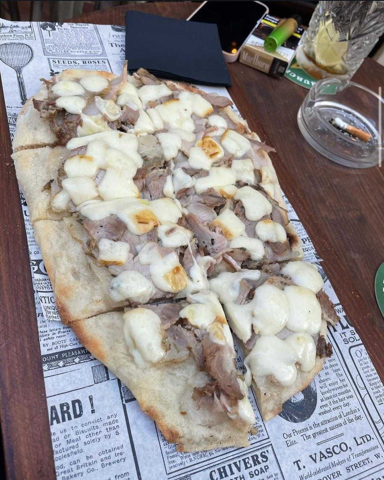 Una pizza con carne y queso está sobre un periódico sobre una mesa.