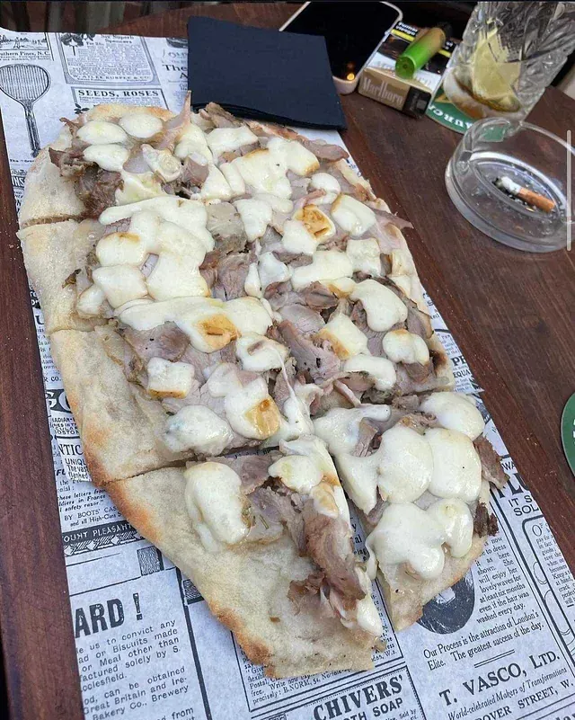 Una pizza con carne y queso está sobre un periódico sobre una mesa.
