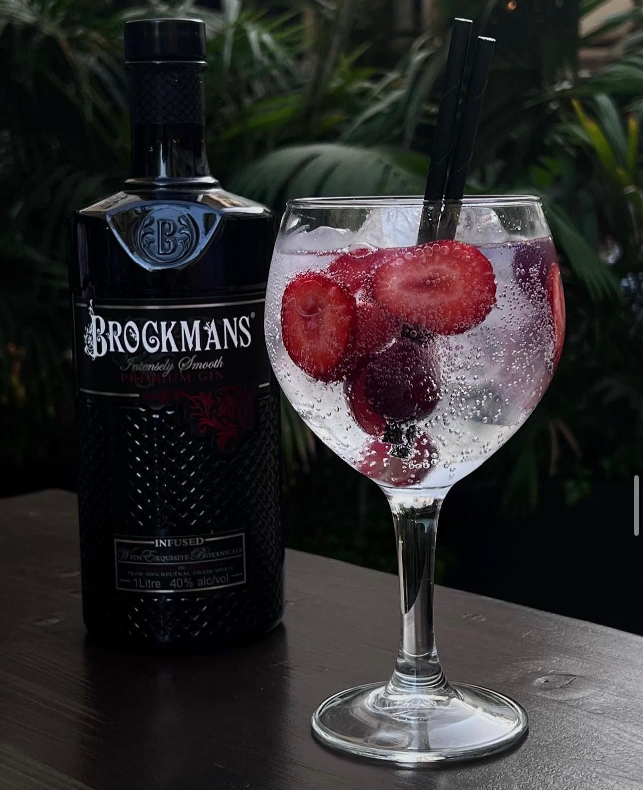 Una botella de ginebra Brockmans y un vaso con fresas.