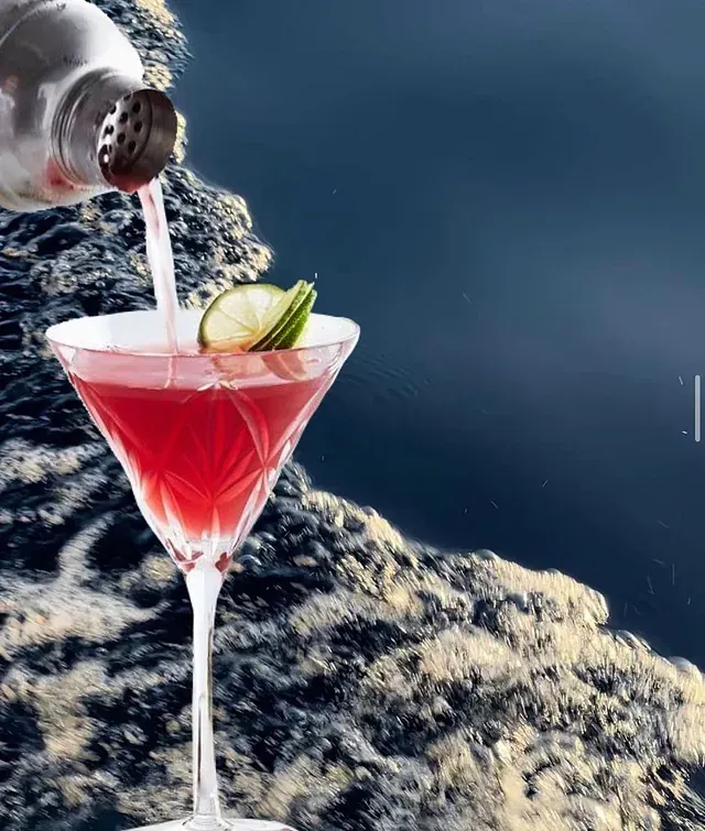 Una persona está vertiendo una bebida roja en una copa de martini.
