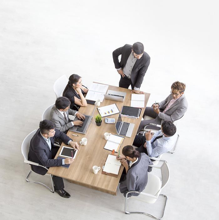 Un grupo de personas están sentadas alrededor de una mesa con computadoras portátiles y cuadernos.