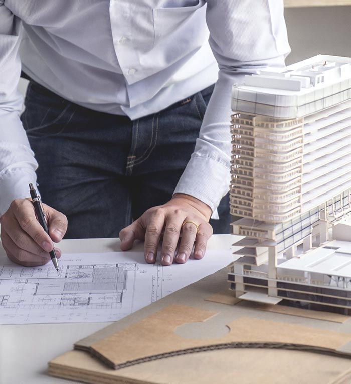 Un hombre está escribiendo en un trozo de papel al lado de una maqueta de un edificio.