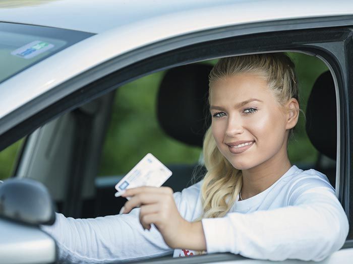 Una mujer está sentada en un coche sosteniendo un permiso de conducir.