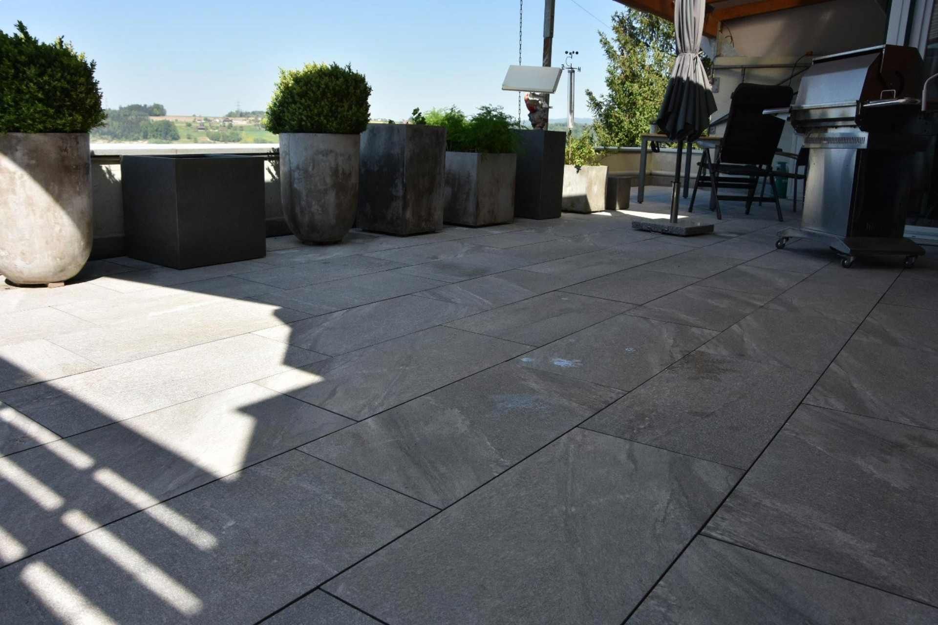 Steinterrasse mit Pflanzkästen und Gartenmöbeln an einem sonnigen Tag.