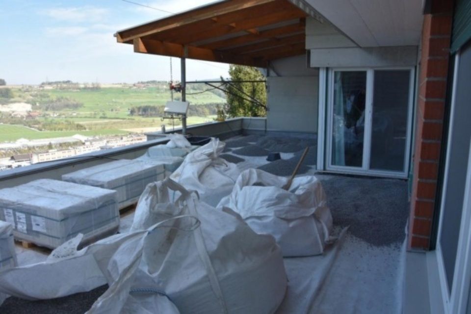 Baumaterialien auf einem Balkon: Säcke und Paletten mit Pflastersteinen. Ländliche Landschaft im Hintergrund.