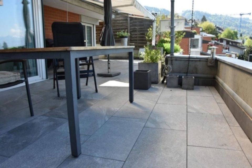 Terrasse mit Tisch, Stühlen und Topfpflanzen mit Blick auf einen Hang.