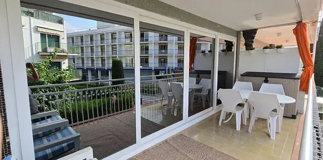 Balcón cubierto con mesa y sillas blancas, hamaca naranja y vistas a los edificios de apartamentos cercanos.