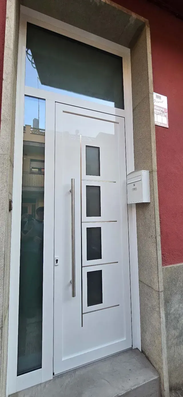 Puerta principal moderna blanca con paneles de vidrio en un portal de piedra en un edificio rojo.
